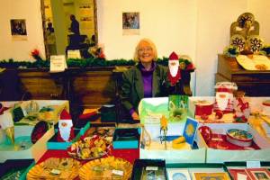 Elisabeth Heilen sitzt hinter ihrem Stand auf dem Adventsmarkt und hält einen Nikolaus in der Hand.
