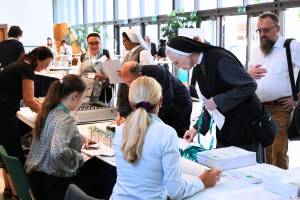 Teilnehmerinnen und Teilnehmer stehen an einem Empfangstisch des Internationalen Kongresses Renovabis in Freising, wo Informationsmaterial und Tagungsunterlagen verteilt werden. Der Kongress fördert den Dialog und die Begegnung zwischen Ost und West.